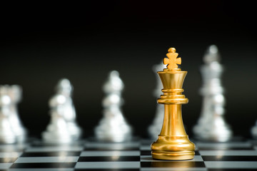 Gold king in chess game face with the another silver team on black background (Concept for company strategy, business victory or decision)