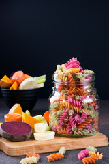 Rice fusilli dry pasta from vegetables in a glass jar. Its natural vegetable dyes celery, beet, carrot, pumpkin, parsnip. Healthy food gluten-free  concept