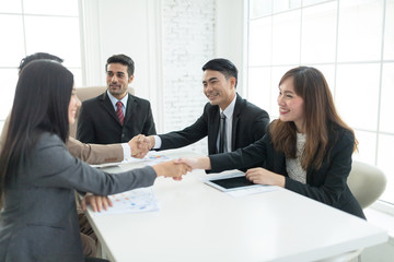 A confident business team of mixed ages and ethnicity making handshaking while meeting in a modern office. They are discussing ideas for their business development.