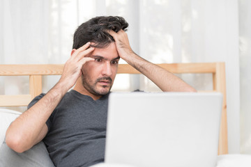 Portrait of Heavy-Hearted Man Looking On Laptop Computer In Bedroom While Massaging His Head. Miserable Unemployed Male Worrying After Checking Stock Market Showing His Nervousness. Feeling exhausted.