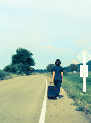 Woman with luggage hitchhiking along a road