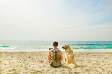 Rear view of man & his dog sitting at beach watching ocean waves, clear sunny day. Fit programmer...