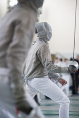 Two teenager fencers fighting with rapiers on the fencing tournament