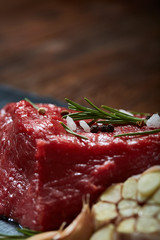 Raw meat beef steaks on black slate board with spices, garlic and rosemary over wooden background, selective focus