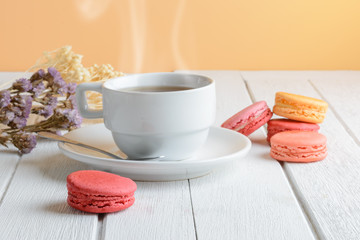 Different types color of macaroons with Cup of hot tea on white wooden background