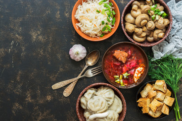 A variety of traditional Russian dishes-borscht,sauerkraut,pickled mushrooms,dumplings. Russian dishes on dark rustic background, top view, copy space.