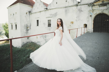 Fototapeta premium Beautiful brunette bride in elegant white dress holding bouquet posing neat trees