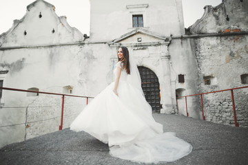 Beautiful elegant bride with perfect wedding dress and bouquet posing near old castle