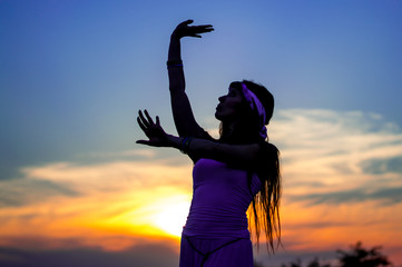 Dark-haired girl in white clothes dancing Oriental dance. Silhouette. Nature. Sunset. Mountainous terrain.