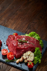 Composition of raw beefsteak on slate board with vegetables and seasoning, selective focus, close-up.