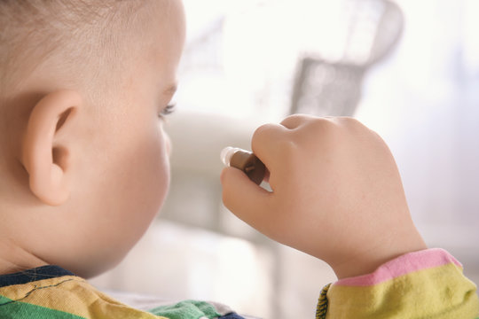 Little girl putting hearing aid in her ear indoors
