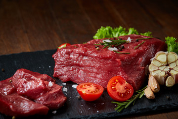 Composition of raw beefsteak on slate board with vegetables and seasoning, selective focus, close-up.