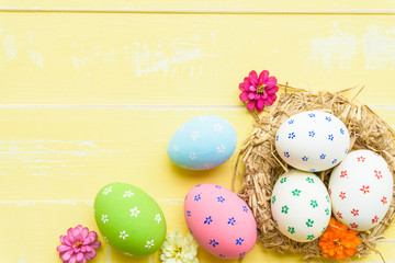 Happy easter! Colorful of Easter eggs in nest with red ribbon, Feather and paper star on pastel color bright yellow and white wooden background.