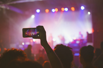 Recording a live show. Fan with hand up takes smartphone video at concert