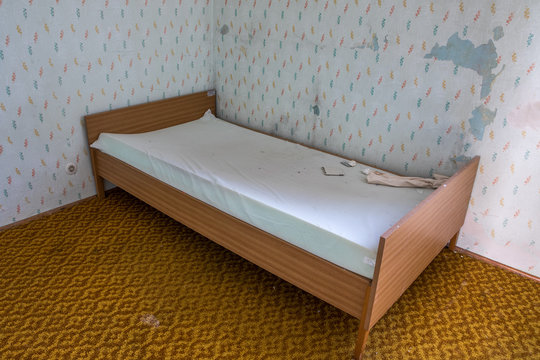 Heruntergekommenes Bett und kaputte Tapete  in renovierungsbedürftigem Zimmer