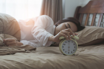 beautiful girl sleeping with hands put on alarm clock for snooze clock wake up on bed in bedroom at holiday morning with sunlight.