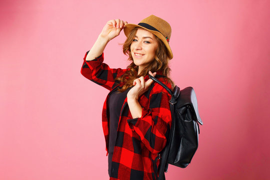 Portrait of young beautiful blond smiley tourist girl holding black suitcase over pink background