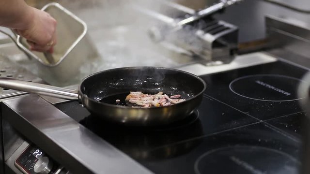 The cook fries bits of bacon in a frying pan