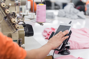 seamstress sews clothes for sewing machine and controls the tablet. textile workshop. closeup