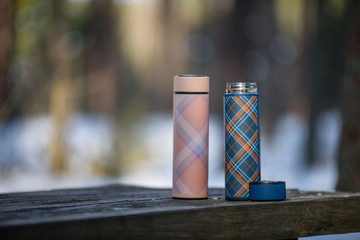 colorful thermoses on wooden table in winter forest