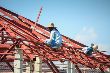 Naklejka premium welder workers installing steel frame structure of the house roof at building construction site