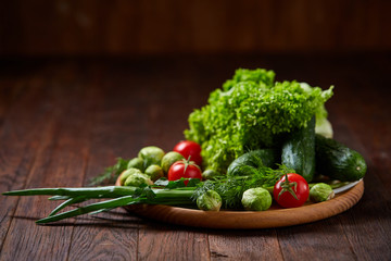 Obraz na płótnie Canvas Vegetarian still life of fresh vegetables on wooden plate over rustic background, close-up, flat lay.