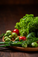 Vegetarian still life of fresh vegetables on wooden plate over rustic background, close-up, flat lay.