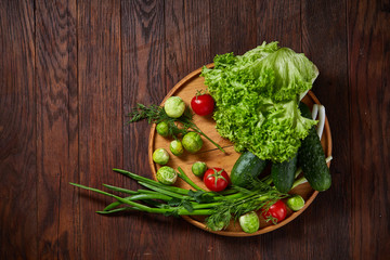 Vegetarian still life of fresh vegetables on wooden plate over rustic background, close-up, flat lay.