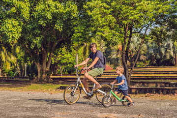 Fototapeta premium Happy family is riding bikes outdoors and smiling. Father on a bike and son on a balancebike
