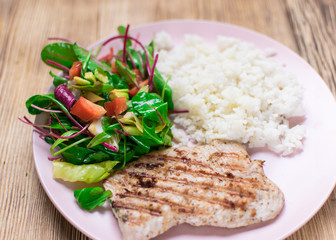 Grilled meat, boiled rice and vegetable salad on a wooden background.
