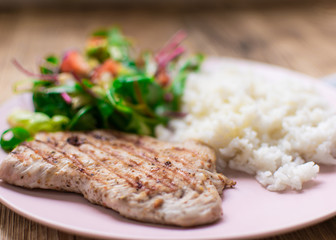 Grilled meat, boiled rice and vegetable salad on a wooden background.