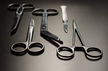 Surgical instruments (three types of scissors, forceps and scalpel) lying on a clean dark monochrome surface in the darkness with a small amount of light