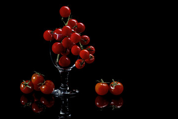 Red tomatoes in a glass, on a black background.