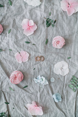 Festive wedding background with pink flower buds, eucalyptus branches, bridal rings, sweets on grey blanket. Flat lay, top view.