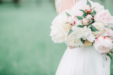 Beauty wedding bouquet of pink and white peony flowers in bride's hands.