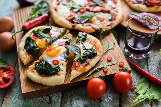 Homemade pizza and wine party. Pizzas with eggs, spinach and chili on oak chopping board over rustic blue background