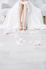 Fototapeta na wymiar Young bride legs in pink high heel shoes and pink flower petals. Festive wedding fashion concept.