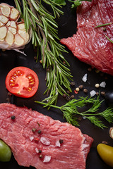 Flat lay of raw beefsteak with vegetables, herbs and spicies on metal tray, close-up, selective focus