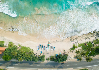 Beautiful beach with turquoise water and fishing boats on the beach. Road on the coast of the ocean. Aerial view, drone photography