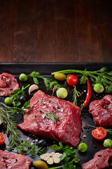 Flat lay of raw beefsteak with vegetables, herbs and spicies on metal tray, close-up, selective focus