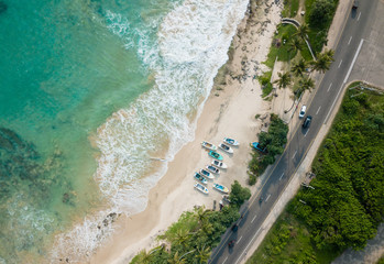Beautiful beach with turquoise water and fishing boats on the beach. Road on the coast of the ocean. Aerial view, drone photography