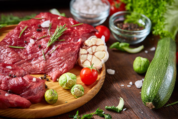 Still life of raw beef meat with vegetables on wooden plate over vintage background, top view, selective focus