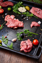 Still life of raw beef meat with vegetables on wooden plate over vintage background, top view, selective focus