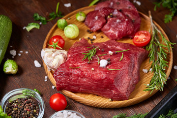 Still life of raw beef meat with vegetables on wooden plate over vintage background, top view, selective focus
