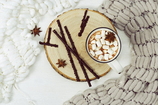 Hot chocolate or cocoa with marshmallows and  chocolate sticks on table with cozy soft knitted fabric with pompons. Holiday concept. Selective focus. Top view.