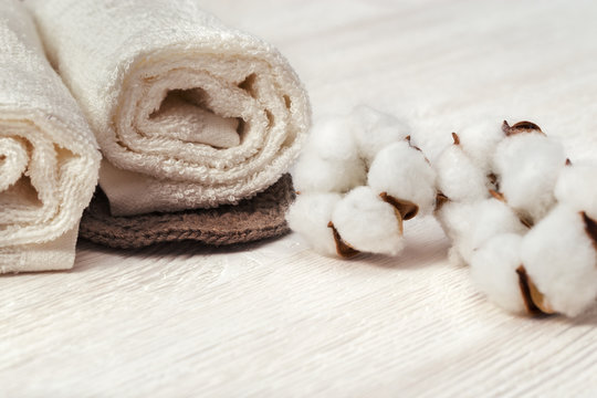 Spa concept. Cotton flower plant and cotton rolled towel on white wooden background with copy space. Toned photo.
