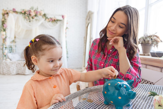 Mom Teaches A Little Daughter To Collect Money In A Piggy Bank