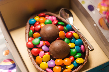 Feliz páscoa com ovo de chocolate confeitado dentro da caixa azul, cheio de confetes e trufas.