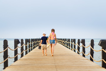Boy and girl walking barefoot along the pier at sea vacation. Summer holidays background