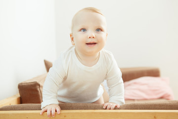 Smiling baby standing at the sofa relying on support.